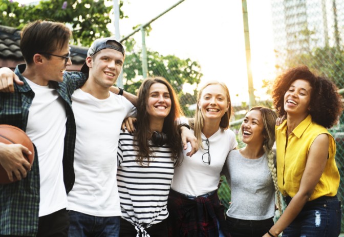 Grupo de jóvenes sonriendo y abrazándose en una cancha al aire libre al atardecer, representando los valores de integración, amistad y alegría promovidos por la FUNDACIÓN ARTÍSTICA DEPORTIVA Y CULTURAL FUNCULTURA 369.
