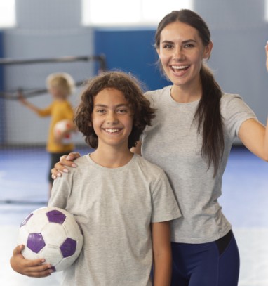 Niño y entrenadora sonriendo en una cancha deportiva, con un balón de fútbol, representando el compromiso de FUNCULTURA 369 con la formación deportiva de calidad para niños y jóvenes.